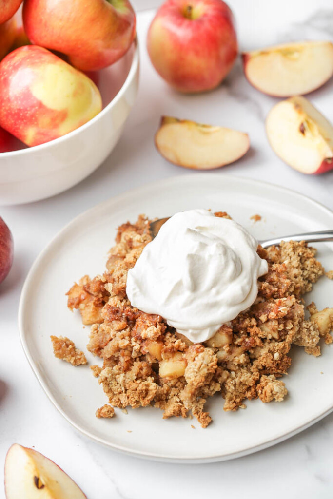 Vegan apple crisp on a plate with a bowl of apples in the background