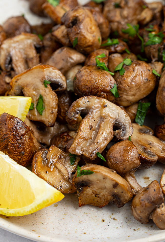 air fryer mushrooms on a plate with fresh parsley and lemon wedges