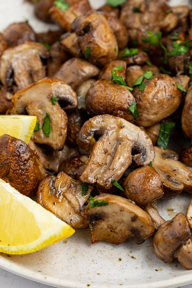 air fryer mushrooms on a plate with fresh parsley and lemon wedges