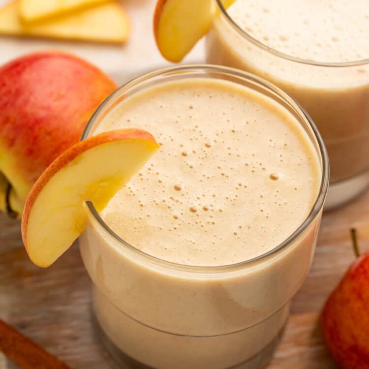 Close up of a pair of apple smoothies; the glasses are garnished with thin apple slices.