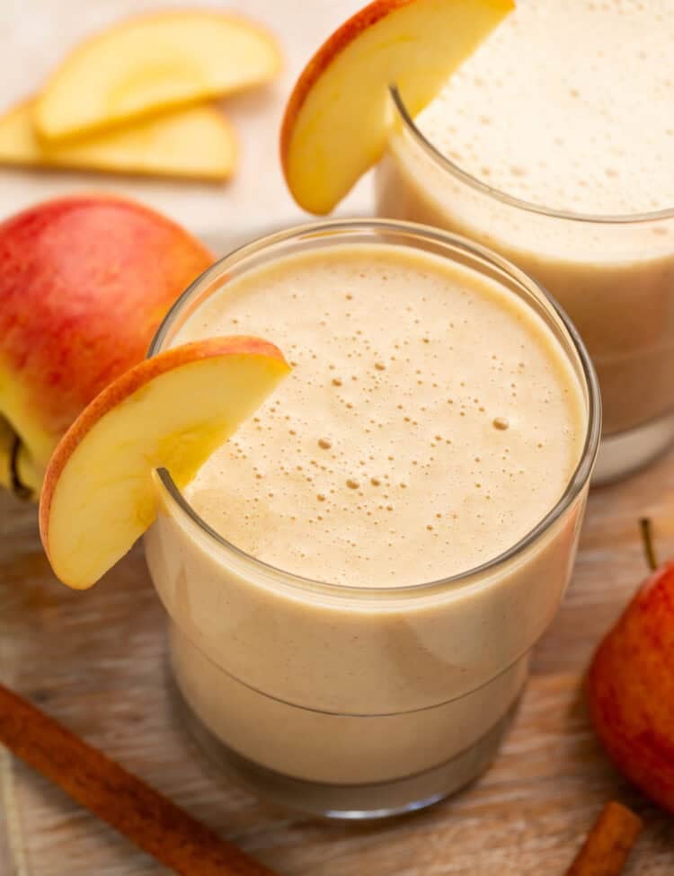 Close up of a pair of apple smoothies; the glasses are garnished with thin apple slices.