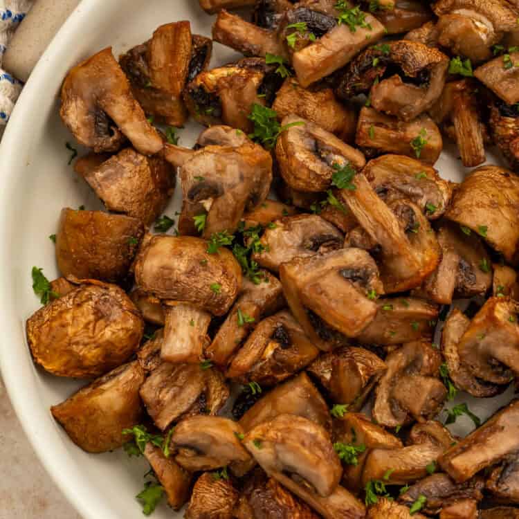 Close up of a white bowl of air fried mushrooms topped with chopped herbs.