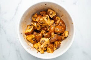 A white bowl full of marinated mushrooms on a white marble counter