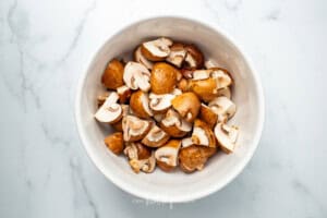 A white bowl full of uncooked and unseasoned mushrooms on a white counter
