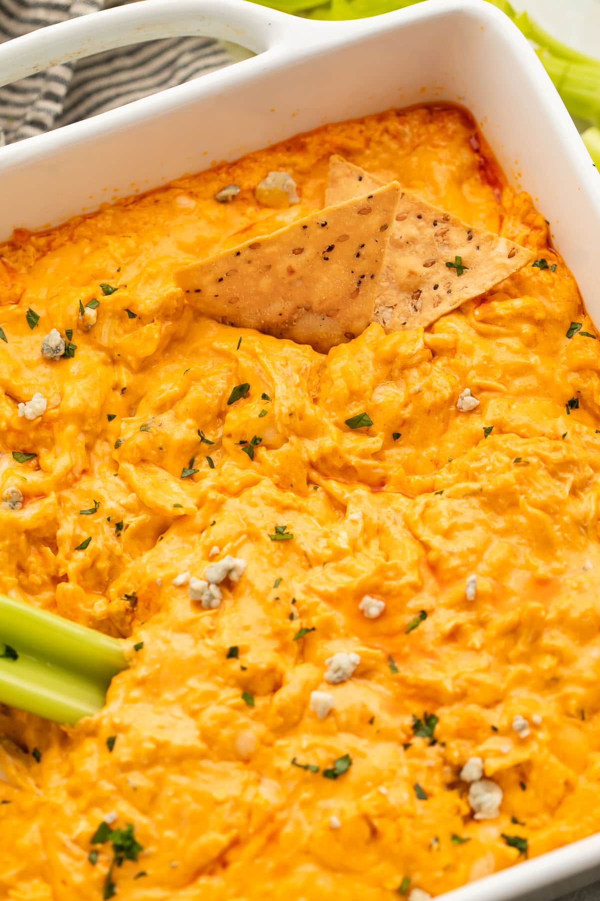 A casserole dish holding keto buffalo chicken dip with a stick of celery and a tortilla chip resting in the dip.