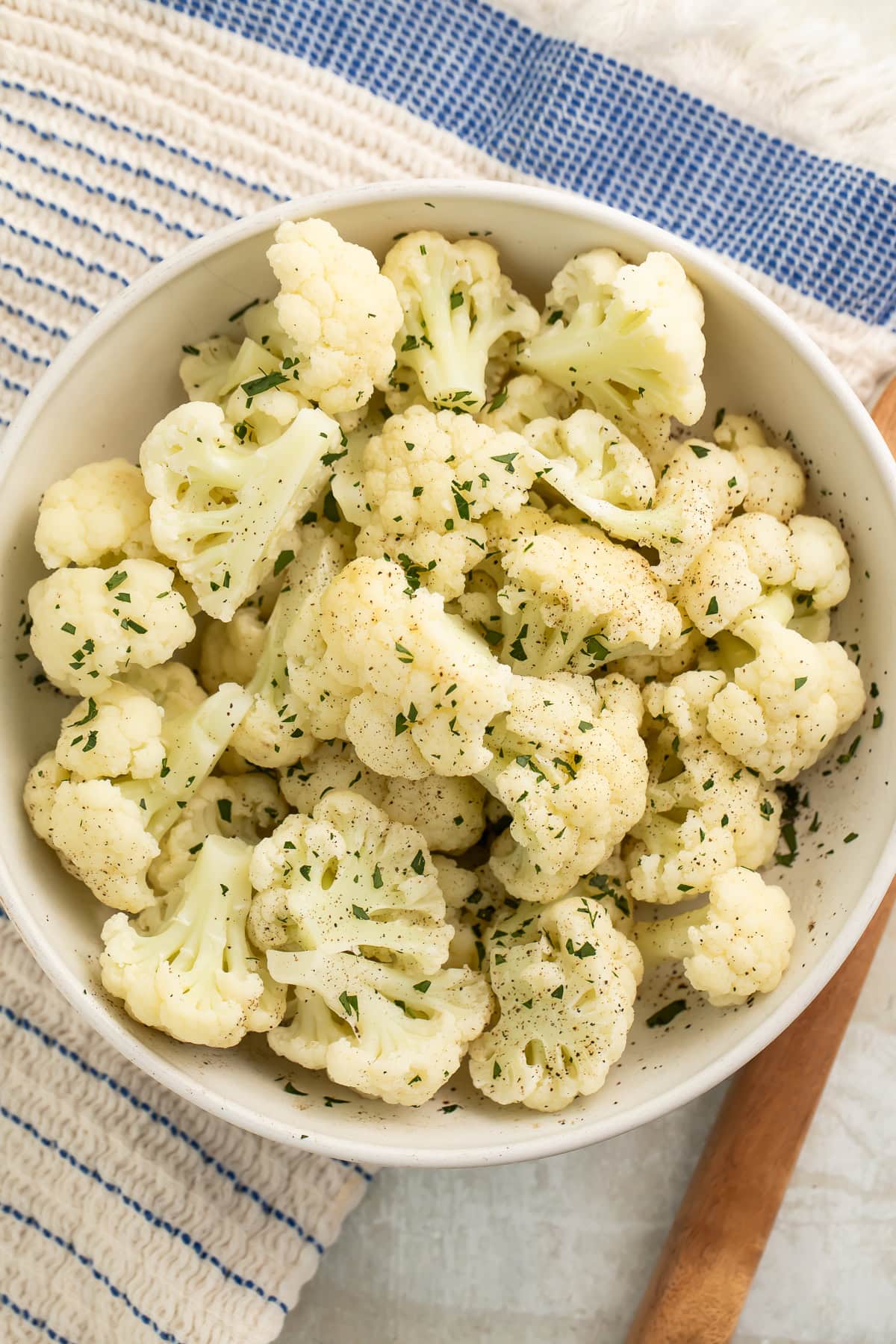 A large white bowl holding Instant Pot Cauliflower seasoned with fresh herbs.