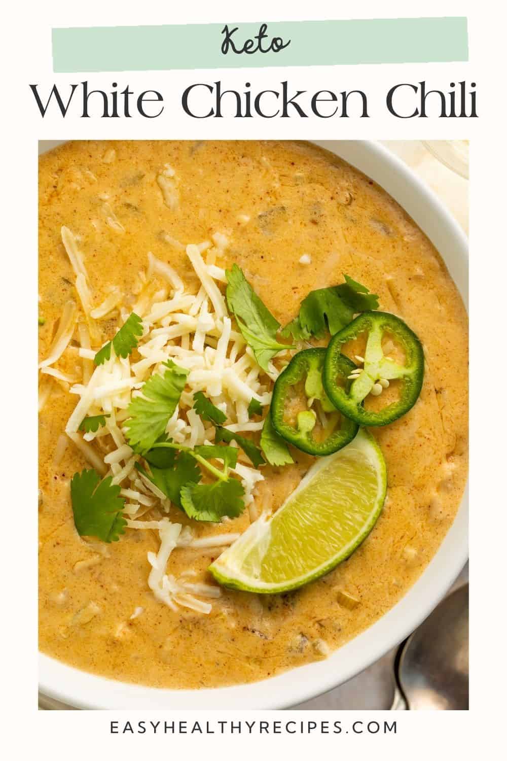 Close up of a bowl of white chicken chili topped with shredded cheese, cilantro, diced jalapeño and a lime wedge, with Pinterest-friendly text overlay.