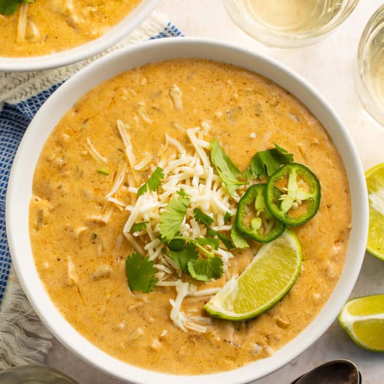 Bowl of white chicken chilli topped with shredded cheese, sliced jalapeno, cilantro and a lime wedge.