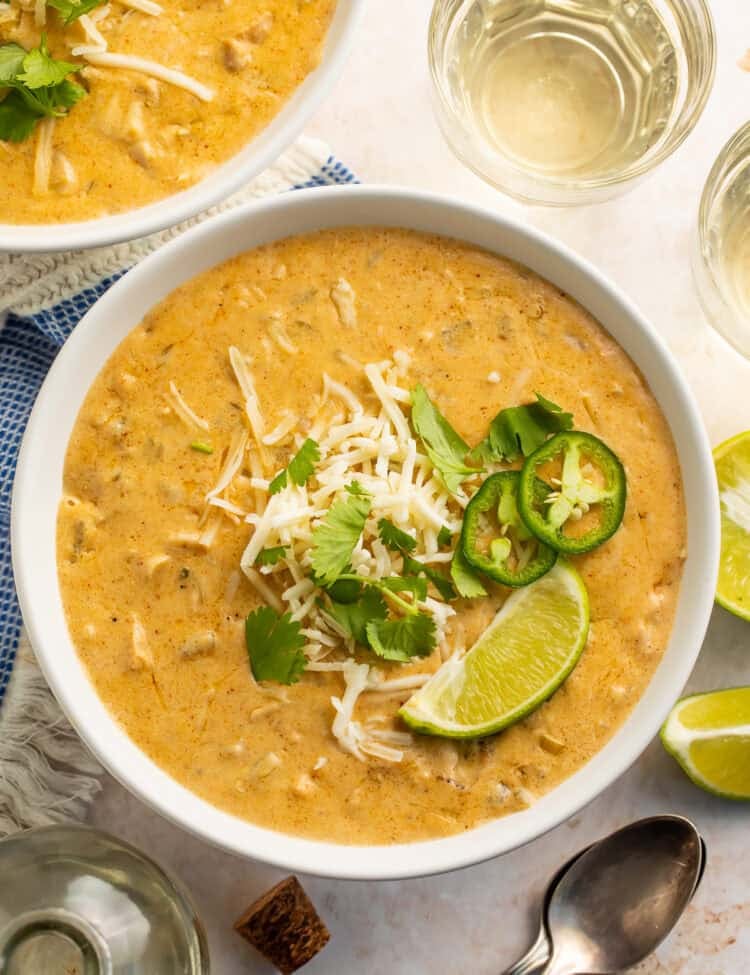 Bowl of white chicken chilli topped with shredded cheese, sliced jalapeno, cilantro and a lime wedge.