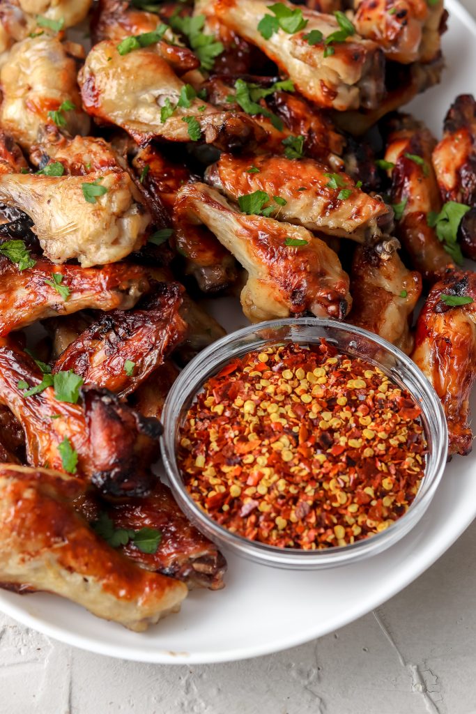 Brine chicken wings on a white plate with a small bowl of red pepper flakes