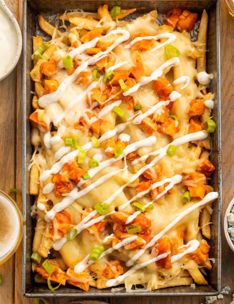 Overhead view of a rectangular baking pan holding french fries topped with buffalo chicken, green onions, and a ranch dressing drizzle.
