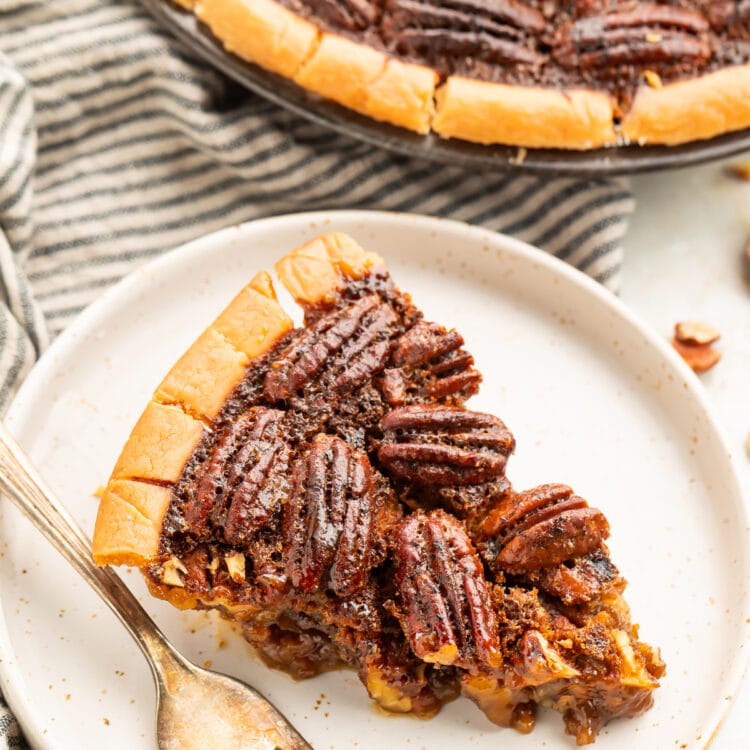 A wedge slice of gluten free pecan pie on a plate next to the remaining pie in a pie plate.