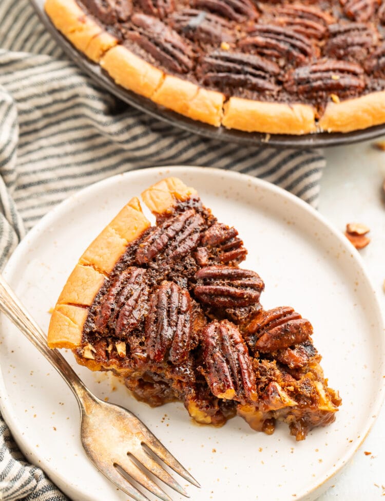 A wedge slice of gluten free pecan pie on a plate next to the remaining pie in a pie plate.