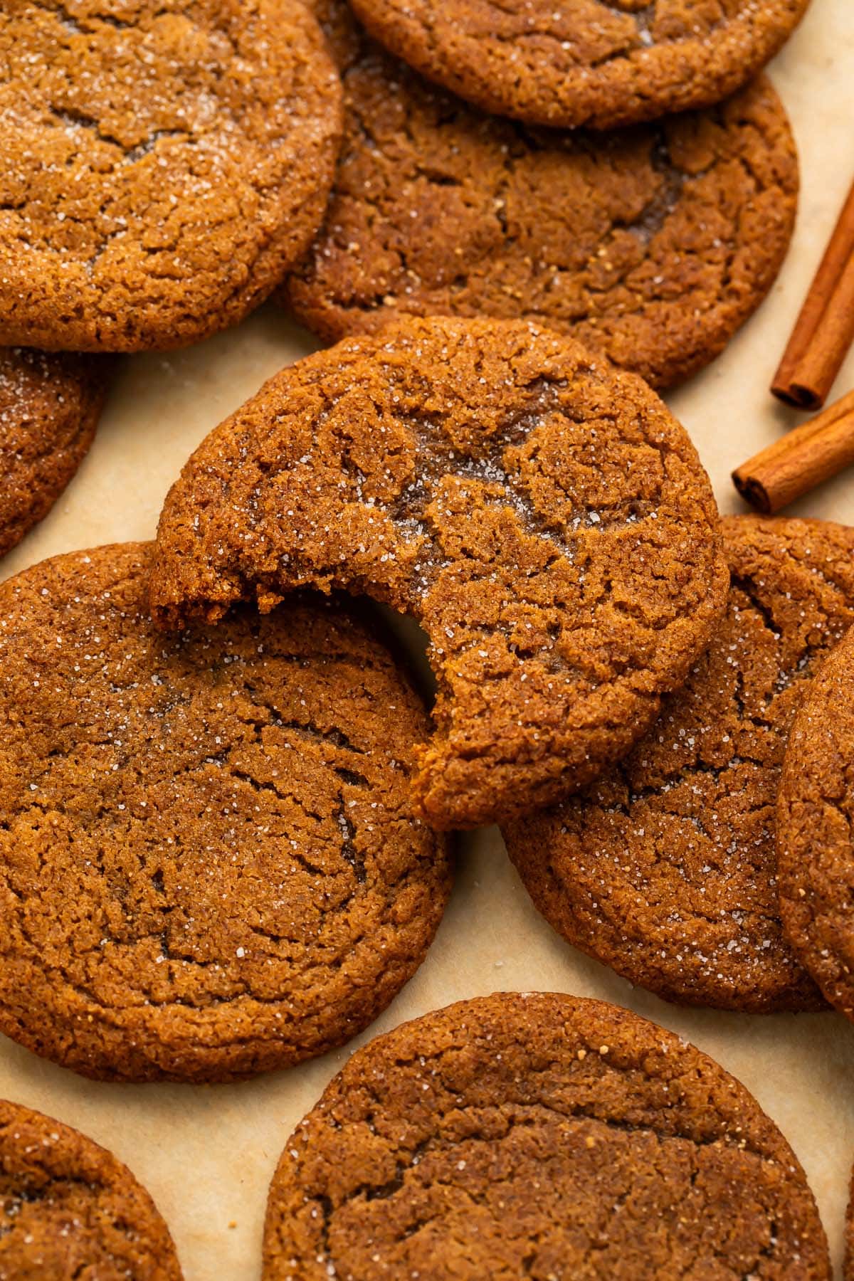 Gluten free ginger snap cookies on a sheet of parchment paper. The topmost cookie has a bite taken out of it.