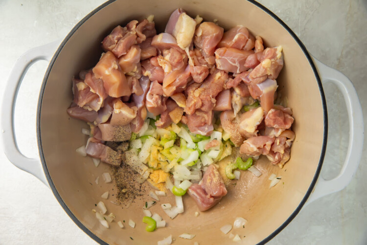 Raw chicken thigh meat, celery, and onions in a large pot