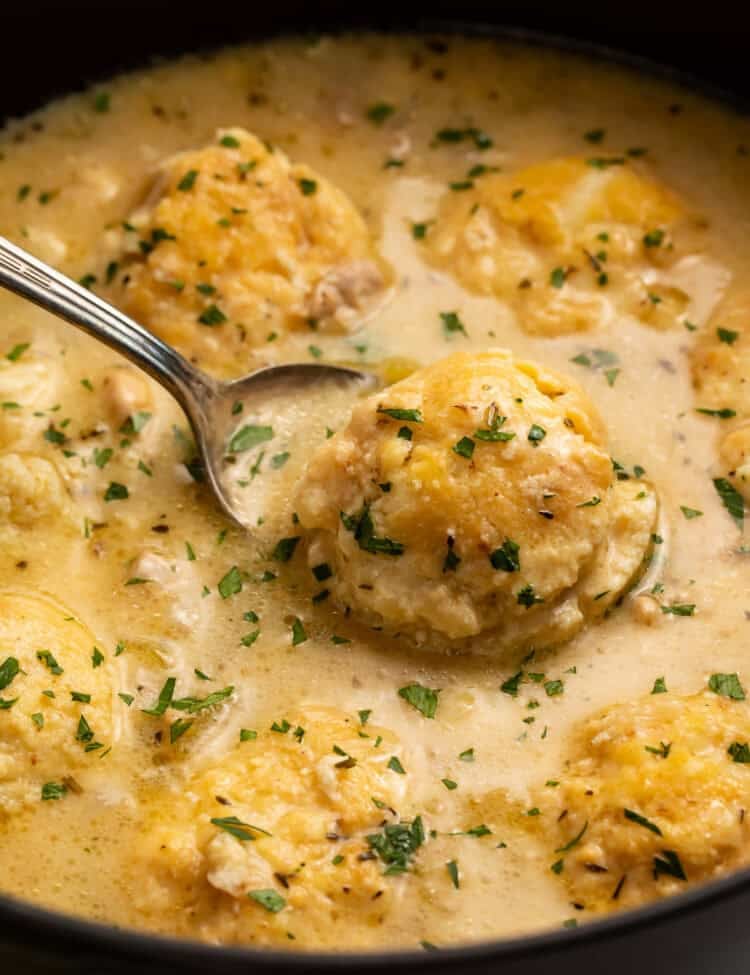 Spoon lifting a dumpling out of a Dutch oven of chicken and dumplings.