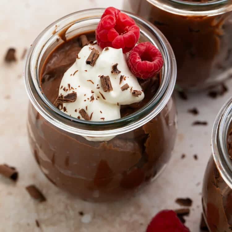 Close up of a pot of keto chocolate pudding topped with fresh raspberries, whipped cream and chocolate shavings.