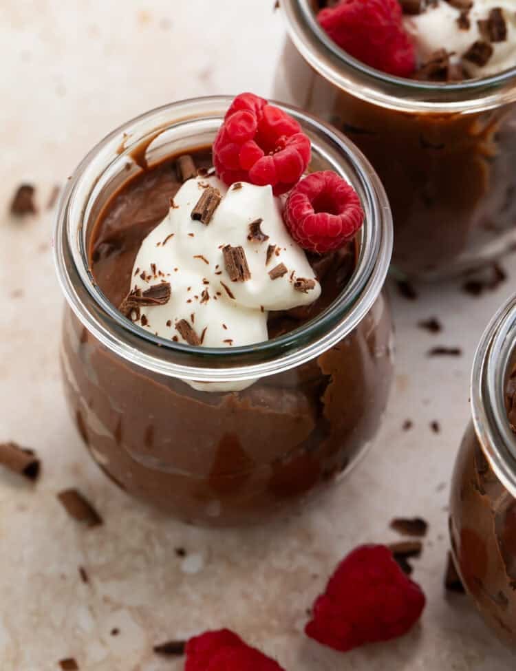 Close up of a pot of keto chocolate pudding topped with fresh raspberries, whipped cream and chocolate shavings.