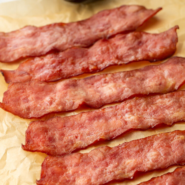 A row of cooked turkey bacon on a sheet of parchment paper in front of a pan.
