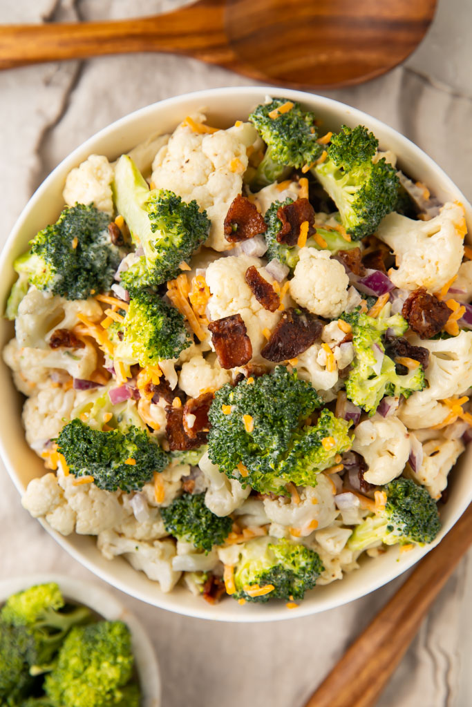 Overhead photo of a white bowl of Amish broccoli salad, with wooden serving utensils