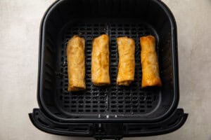 4 frozen egg rolls in an air fryer basket