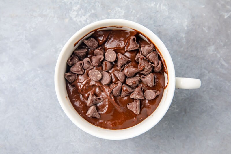 Top-down view of chocolate gluten-free mug cake batter topped with chocolate chips in a white mug.