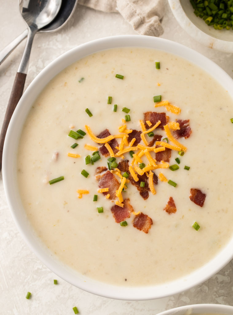 Irish potato soup topped with bacon, chives, and shredded cheddar cheese in a white bowl on a table