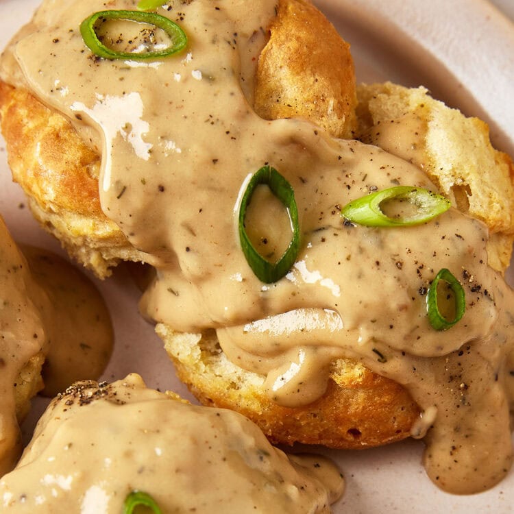 Vegan biscuits and gravy topped with sliced green onions on a plate.