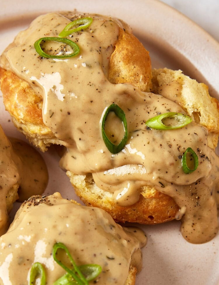Vegan biscuits and gravy topped with sliced green onions on a plate.