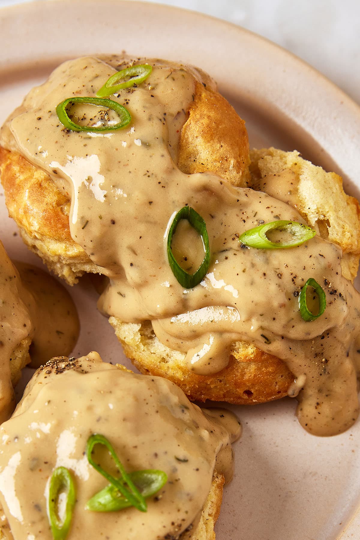 Vegan biscuits and gravy topped with sliced green onions on a plate.