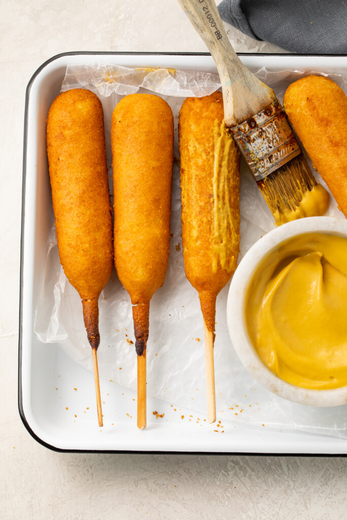 Air fryer corn dogs on a tray next to a bowl of mustard