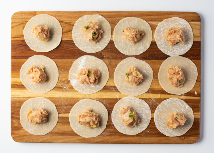Wonton wrappers on a cutting board, filled with chicken gyoza filling