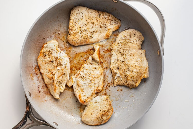 Chicken cutlets in a large grey skillet.