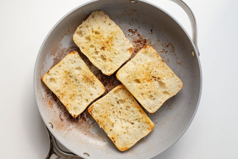 Halved ciabatta rolls in a large grey skillet.