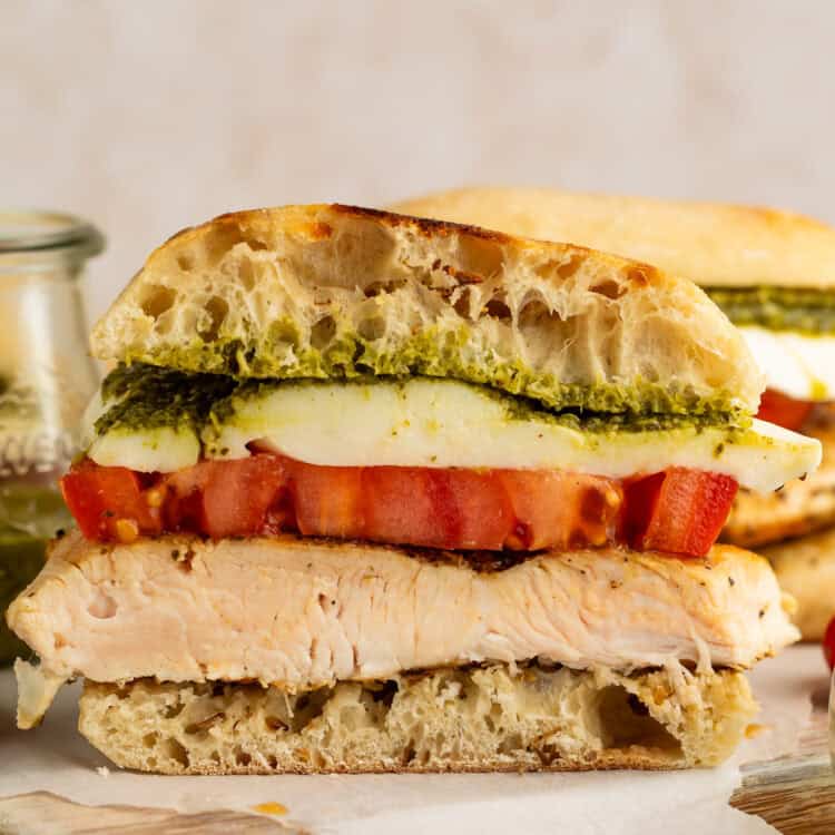 Side on close up of a sliced chicken sandwich with pesto, mozzarella and tomato.