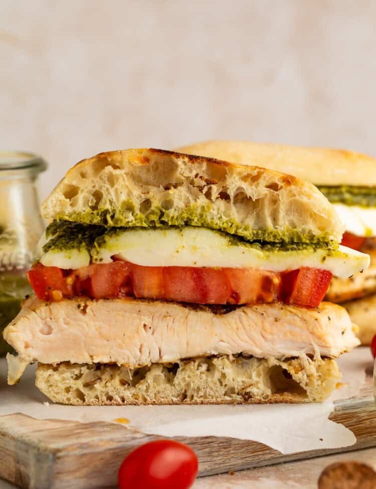 Side on close up of a sliced chicken sandwich with pesto, mozzarella and tomato.