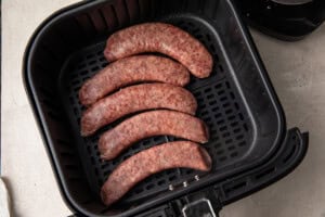 Uncooked sausages in an air fryer basket