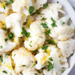 Overhead photo of a bowl of steamed cauliflower garnished with lemon zest and chopped parsley