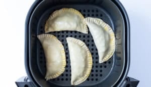 Unbaked empanadas in an air fryer basket