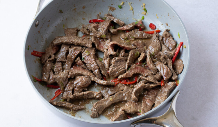 Thinly sliced beef in skillet with garlic and red chilis