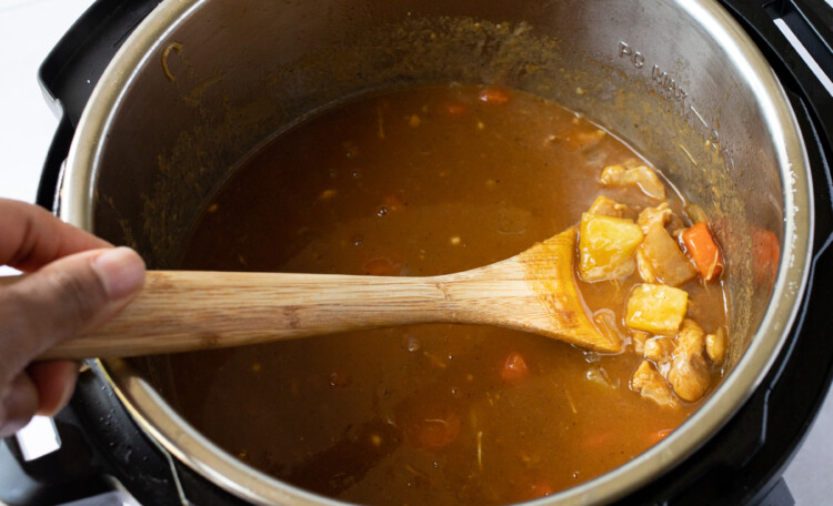 A close up photo of Japanese curry in the Instant Pot with a wooden spoon