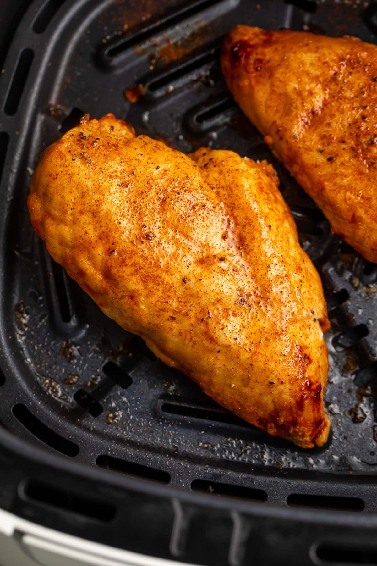 A previously frozen chicken breast in an air fryer basket.