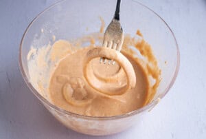 Coated onion ring held over batter in a large glass mixing bowl with a fork