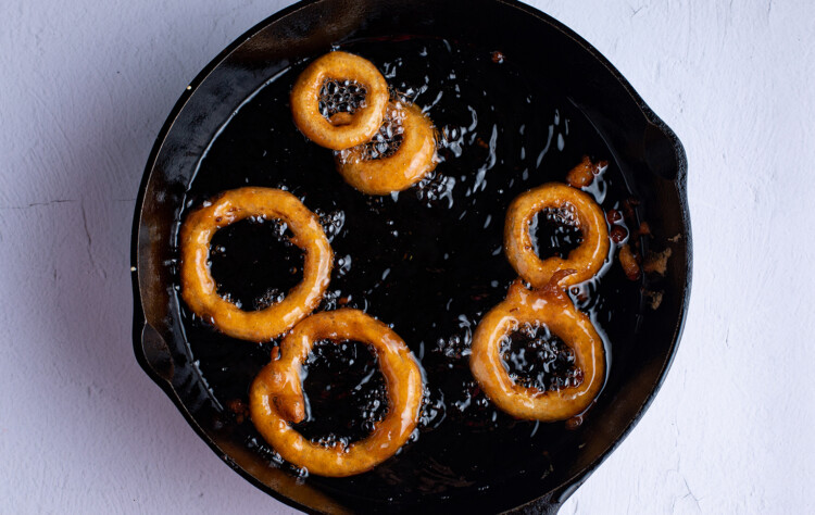 Gluten free onion rings frying in oil in a large cast iron skillet
