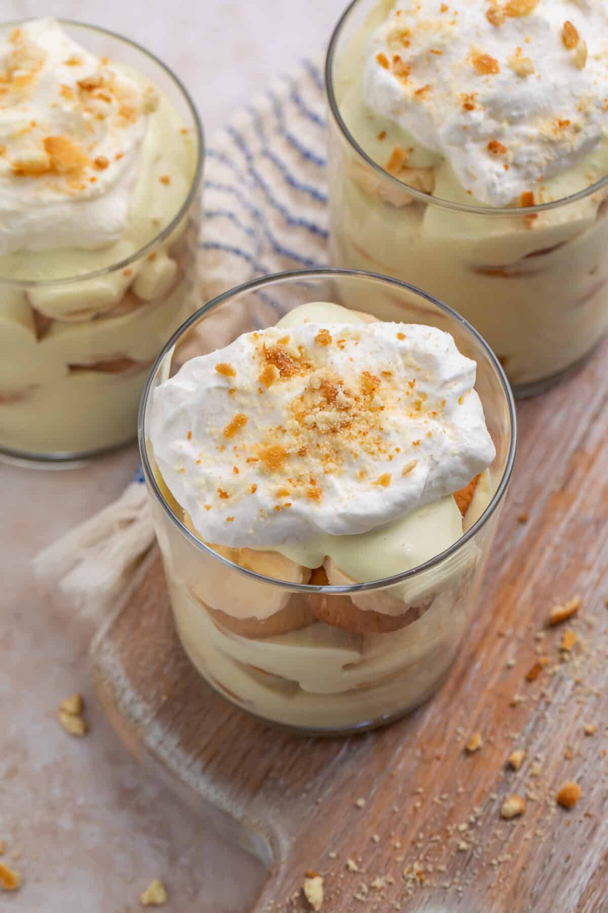 Side on view of individual vegan banana puddings topped with whipped topping and crumbled wafers.