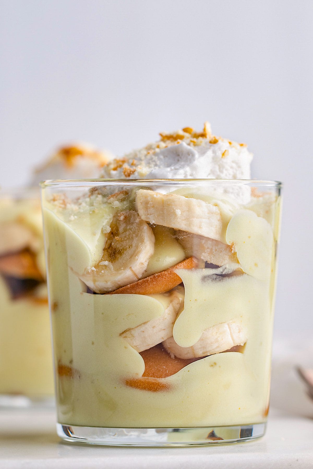 Side view of a short glass holding vegan banana pudding layered with slices of bananas and Nilla wafers.