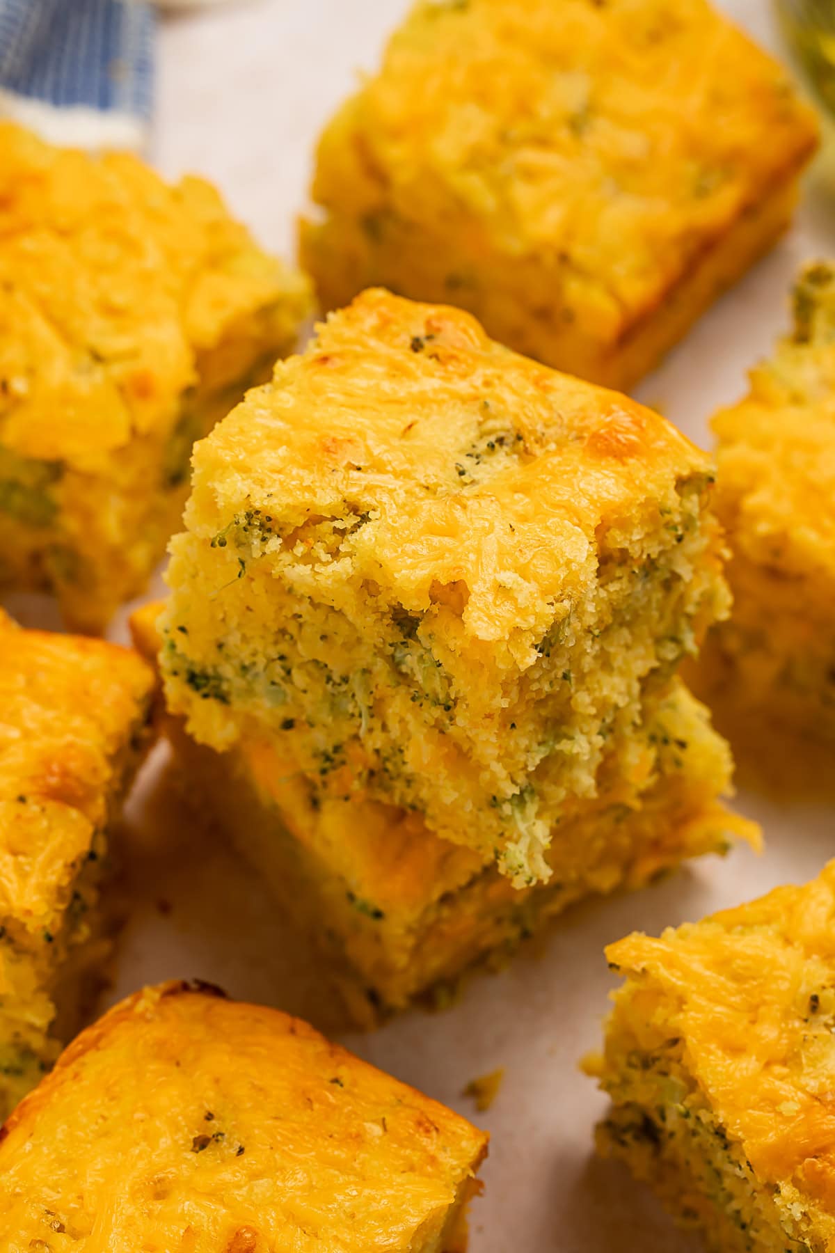 Overhead, angled photo of a square of broccoli cornbread on top of another square of cornbread, surrounded by other squares of cornbread.