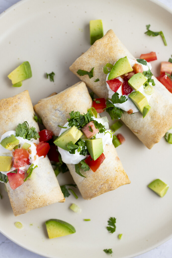 Frozen burritos cooked in the air fryer topped with pico, guacamole, and sour cream