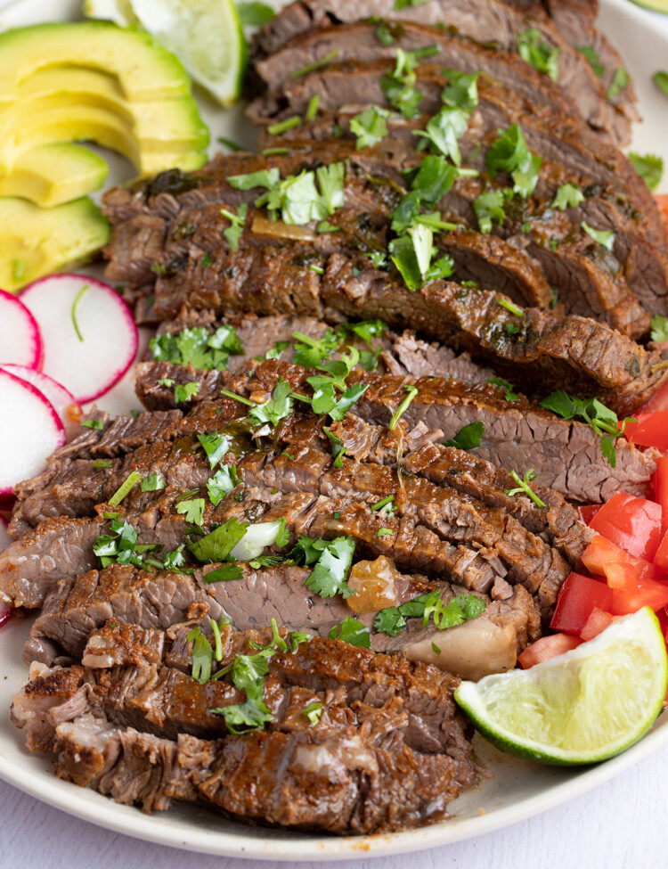 Sliced Instant Pot carne asada on a white plate surrounded by vegetables