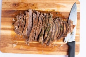 Sliced flank steak on a cutting board with a sharp knife